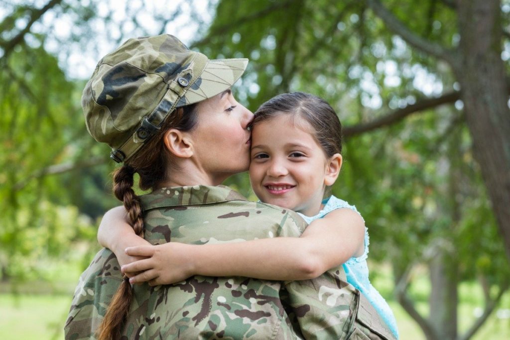 Woman in a military uniform holds a young girl who is smiling.