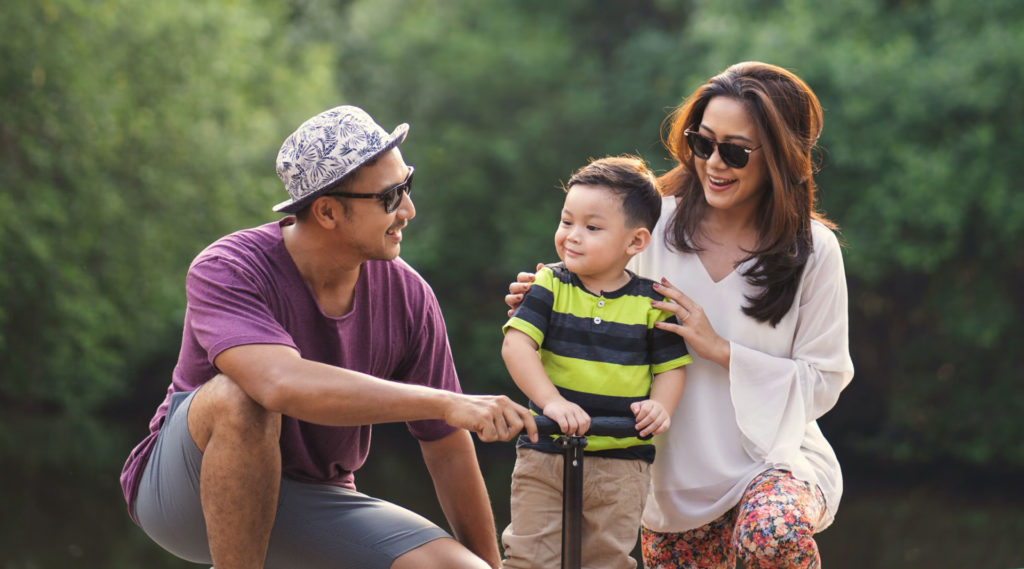 A couple holding a boy who is riding a skateboard