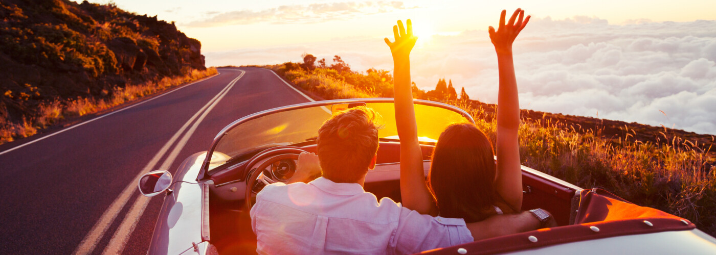 Couple in classic car driving towards sunset